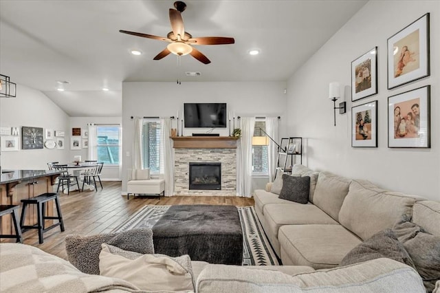 living area featuring wood finished floors, visible vents, a ceiling fan, a fireplace, and vaulted ceiling