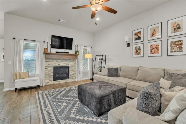 living room with visible vents, a ceiling fan, wood finished floors, a stone fireplace, and baseboards