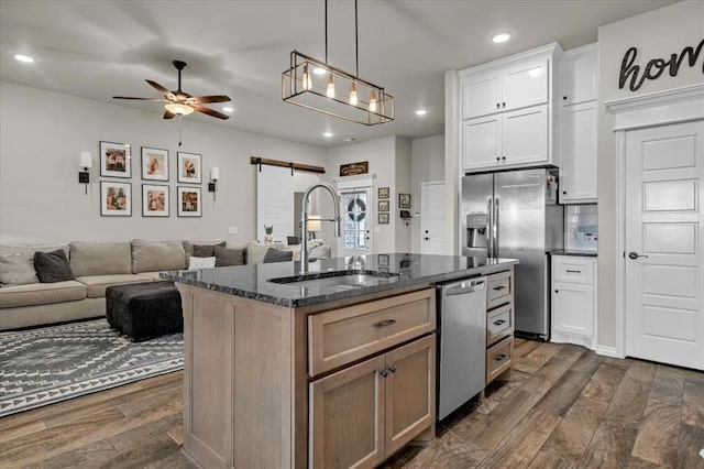 kitchen featuring dark stone countertops, dark wood finished floors, stainless steel appliances, a sink, and a barn door