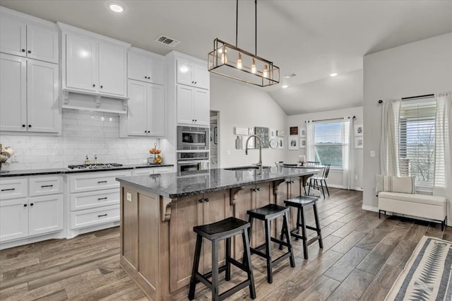 kitchen featuring tasteful backsplash, stainless steel appliances, wood finished floors, white cabinetry, and a sink