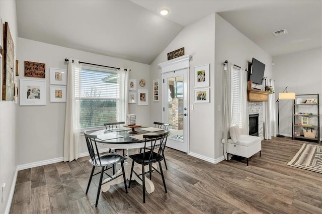 dining room featuring visible vents, baseboards, lofted ceiling, a fireplace, and wood finished floors