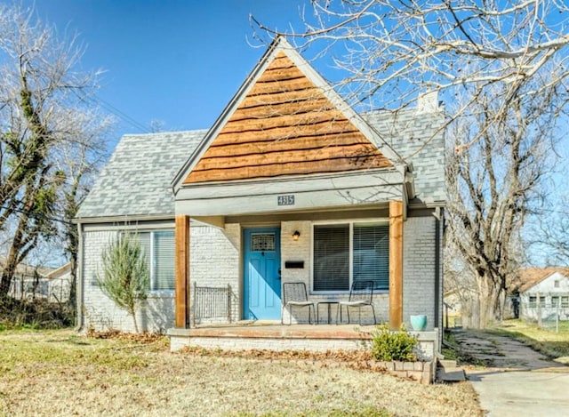 bungalow featuring brick siding, covered porch, and roof with shingles