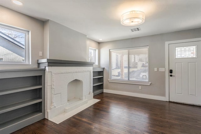 unfurnished living room featuring visible vents, plenty of natural light, wood finished floors, and a fireplace