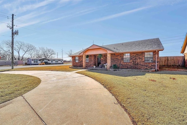 ranch-style house with brick siding, a front lawn, fence, roof with shingles, and driveway