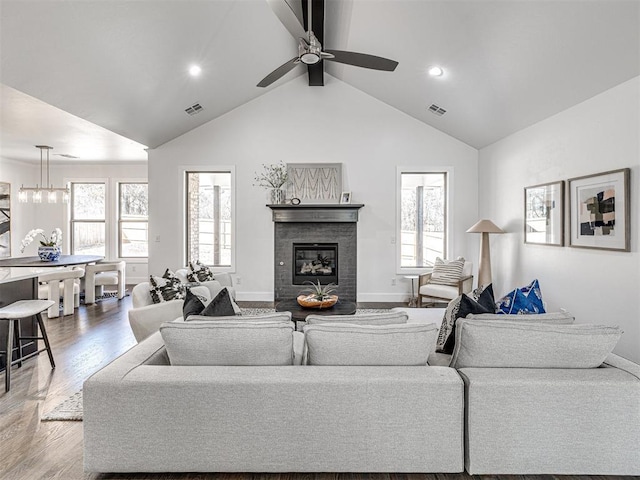 living room with ceiling fan with notable chandelier, wood finished floors, visible vents, and a tile fireplace