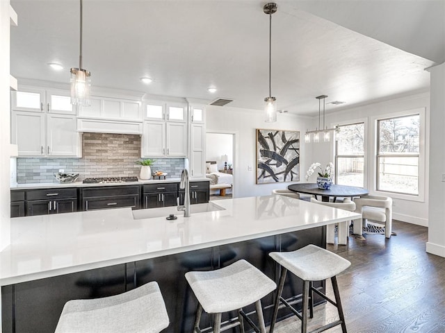 kitchen with backsplash, light countertops, stainless steel gas stovetop, white cabinets, and a sink