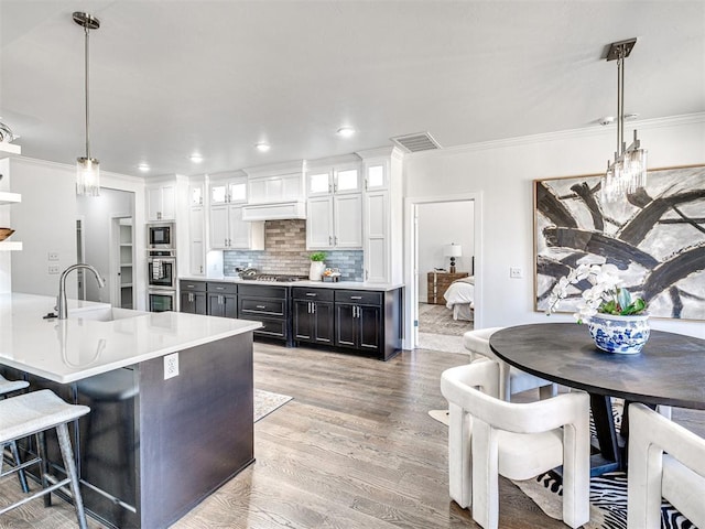 kitchen featuring visible vents, stainless steel appliances, a sink, light wood-style floors, and tasteful backsplash