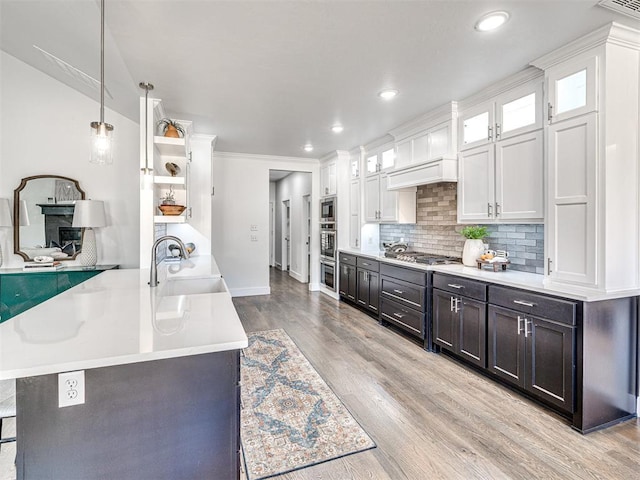 kitchen with light wood-type flooring, a sink, open shelves, light countertops, and decorative backsplash