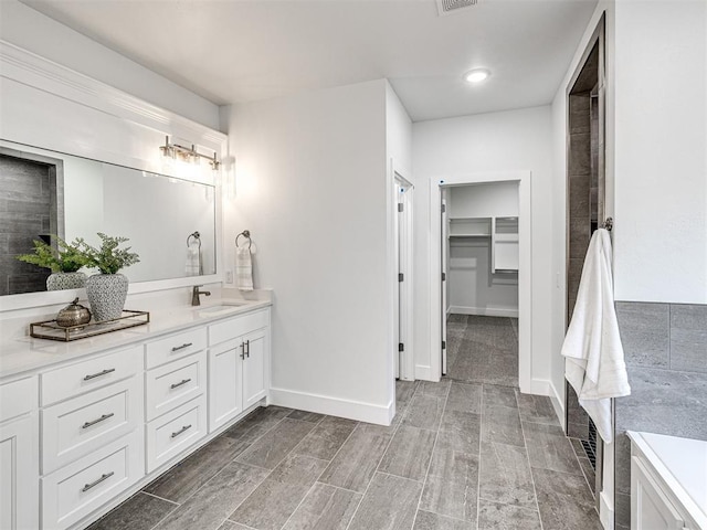 full bathroom with vanity, a walk in closet, baseboards, and visible vents