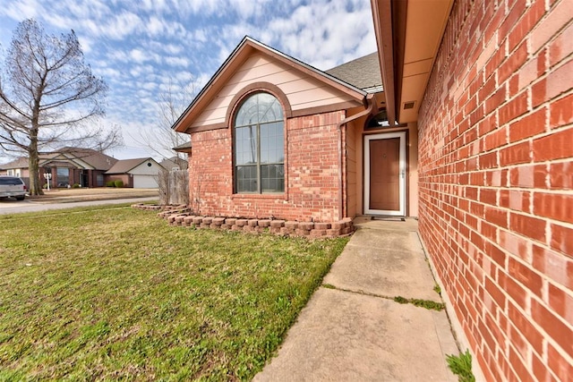 doorway to property featuring brick siding and a lawn