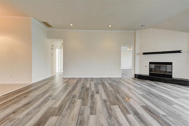 unfurnished living room with wood finished floors, visible vents, baseboards, crown molding, and a brick fireplace