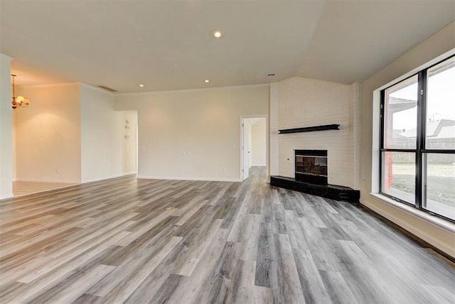 unfurnished living room featuring wood finished floors, a fireplace, baseboards, a chandelier, and vaulted ceiling