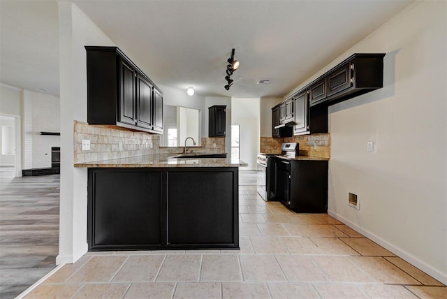 kitchen with stainless steel electric stove, a peninsula, decorative backsplash, light stone countertops, and dark cabinets