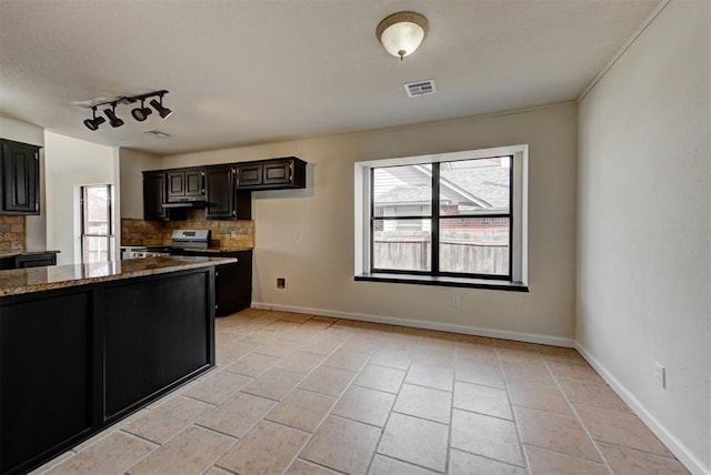 kitchen featuring a wealth of natural light, decorative backsplash, stone counters, and electric stove