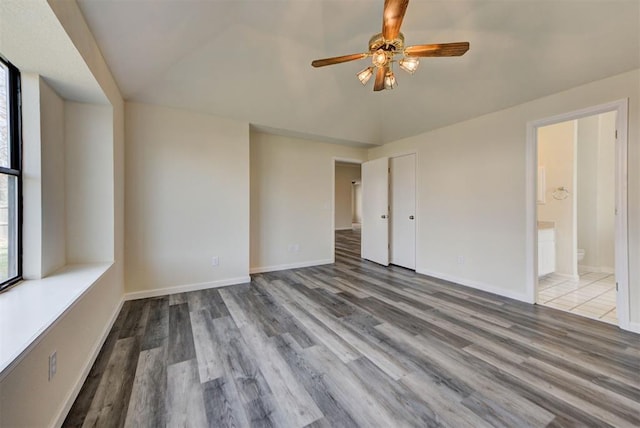 unfurnished bedroom with vaulted ceiling, ensuite bath, baseboards, and wood finished floors