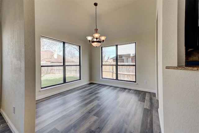 unfurnished dining area with a notable chandelier, lofted ceiling, dark wood finished floors, baseboards, and a textured wall