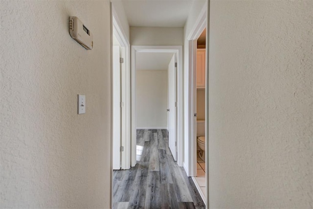 corridor featuring wood finished floors and a textured wall