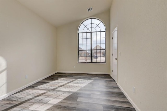 spare room featuring visible vents, wood finished floors, baseboards, and vaulted ceiling