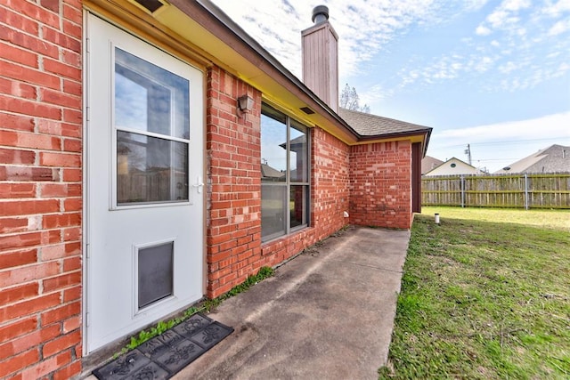 doorway to property with fence, a yard, a shingled roof, a chimney, and brick siding