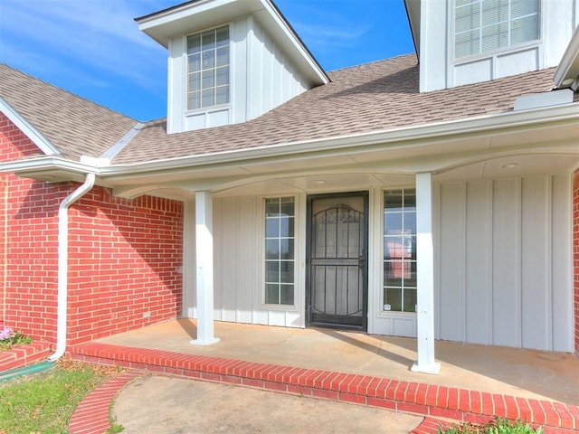 entrance to property with board and batten siding, covered porch, brick siding, and a shingled roof