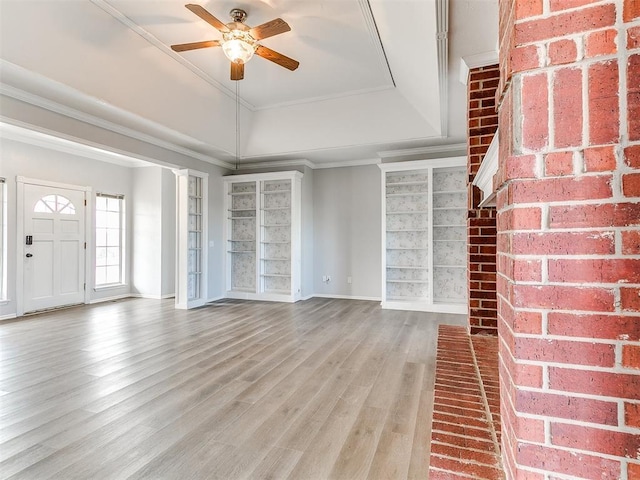 unfurnished living room featuring built in shelves, a ceiling fan, wood finished floors, baseboards, and ornamental molding