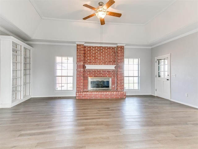 unfurnished living room featuring plenty of natural light, a brick fireplace, wood finished floors, and crown molding