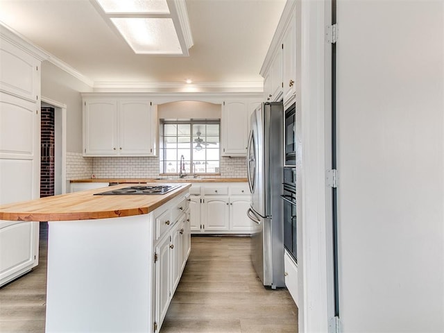 kitchen with backsplash, cooktop, butcher block countertops, freestanding refrigerator, and white cabinets