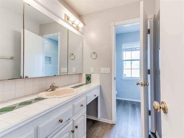 bathroom with vanity, wood finished floors, baseboards, decorative backsplash, and toilet