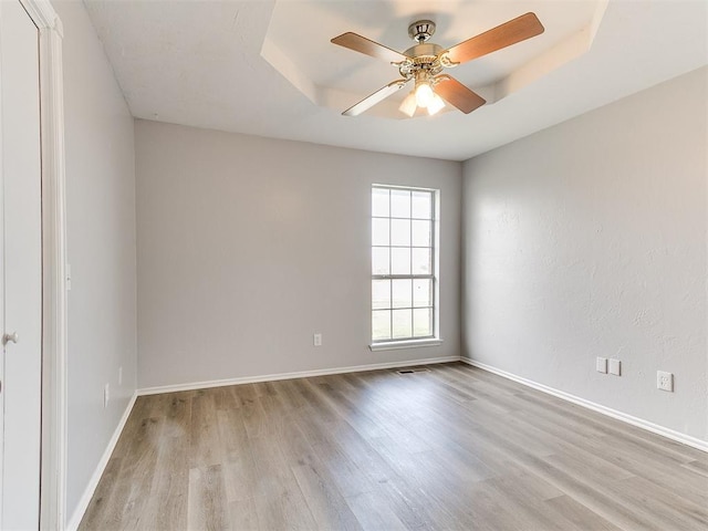 unfurnished room featuring visible vents, a raised ceiling, a ceiling fan, wood finished floors, and baseboards