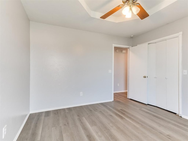 unfurnished bedroom featuring a tray ceiling, baseboards, a closet, and wood finished floors