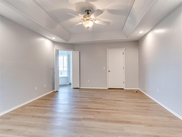 spare room featuring a tray ceiling, baseboards, ornamental molding, and light wood finished floors