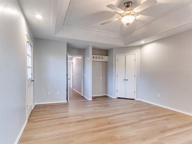 unfurnished bedroom featuring a tray ceiling, attic access, baseboards, and light wood finished floors