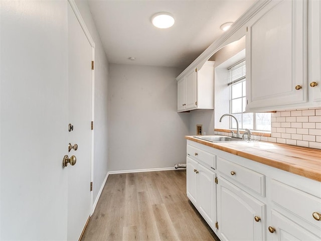 kitchen with a sink, backsplash, white cabinets, light wood finished floors, and wooden counters