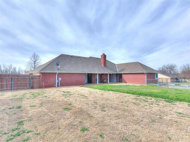 back of property featuring brick siding, a chimney, a yard, and fence