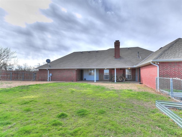 rear view of house with a lawn, a chimney, brick siding, and fence