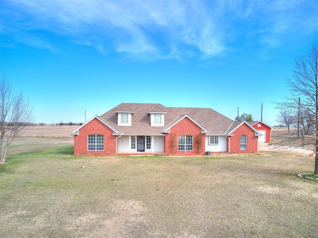 view of front of home with brick siding, a front yard, and a shingled roof