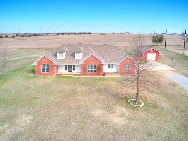 view of front of property with an outbuilding, a detached garage, a rural view, a front yard, and brick siding