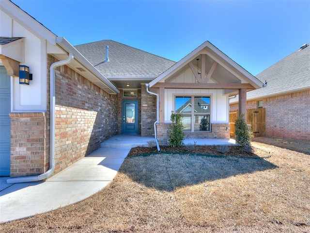 view of exterior entry with a garage, brick siding, board and batten siding, and a shingled roof