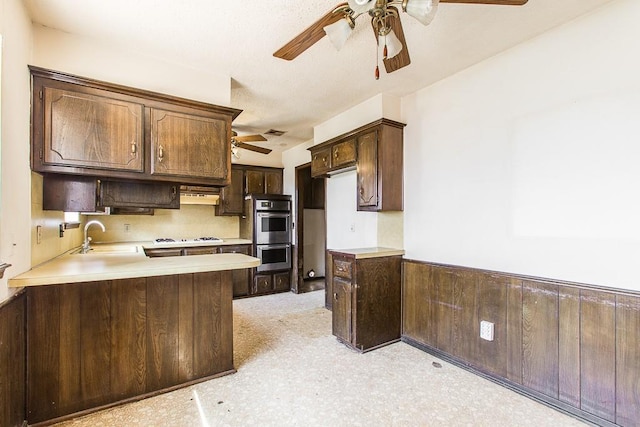 kitchen with a sink, double oven, dark brown cabinets, and light countertops