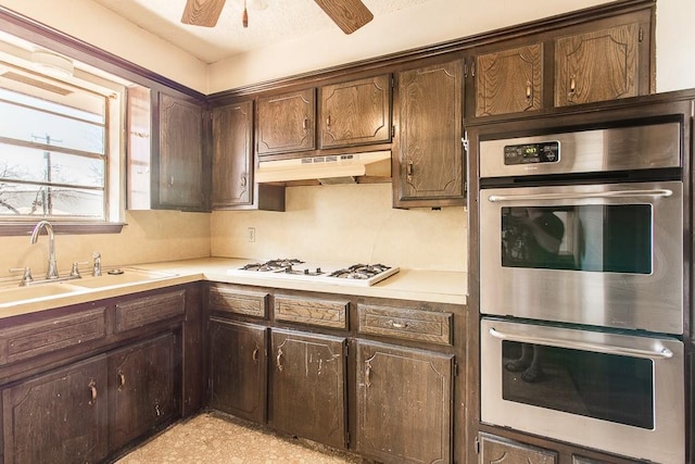 kitchen featuring under cabinet range hood, a sink, double oven, dark brown cabinetry, and light countertops