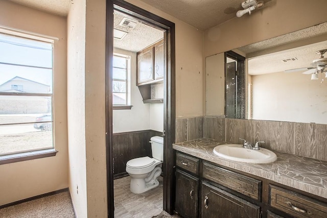 half bathroom with vanity, a textured ceiling, wainscoting, and toilet