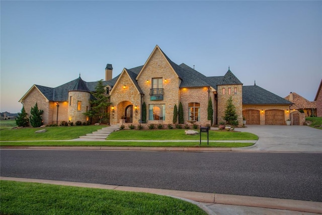 french country style house featuring a front yard, a chimney, concrete driveway, a garage, and stone siding