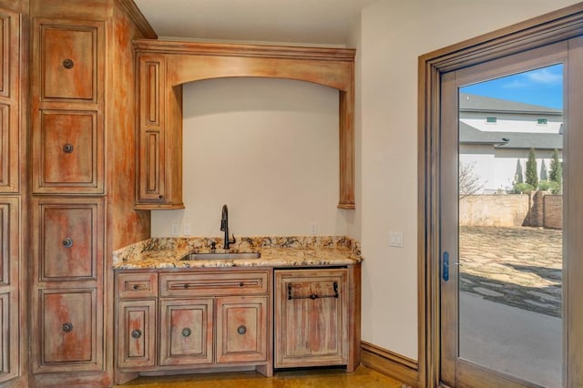 interior space featuring brown cabinets, light stone countertops, baseboards, and a sink