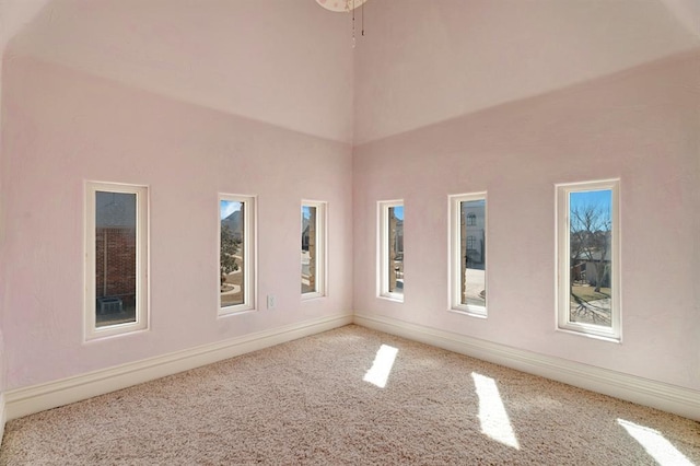 carpeted empty room featuring a high ceiling and baseboards