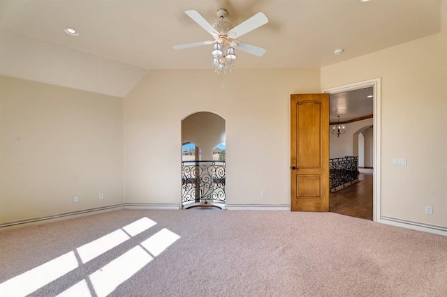 empty room featuring baseboards, ceiling fan, vaulted ceiling, carpet floors, and arched walkways