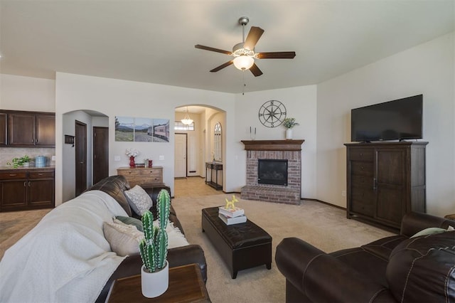 living room with a ceiling fan, baseboards, a fireplace, arched walkways, and light colored carpet