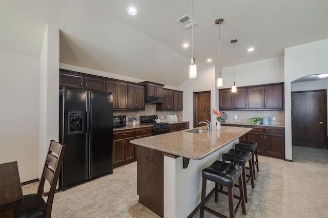 kitchen featuring visible vents, a center island with sink, arched walkways, black appliances, and dark brown cabinets