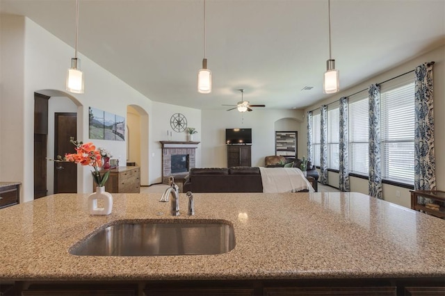 kitchen featuring a sink, arched walkways, a fireplace, and light stone countertops