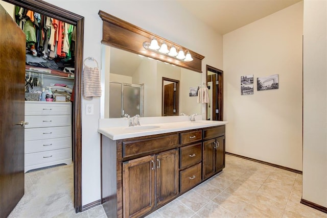 full bath featuring double vanity, a shower with door, baseboards, and a sink