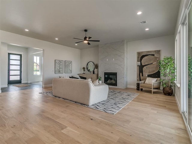 living room with a high end fireplace, ceiling fan, light wood finished floors, baseboards, and visible vents